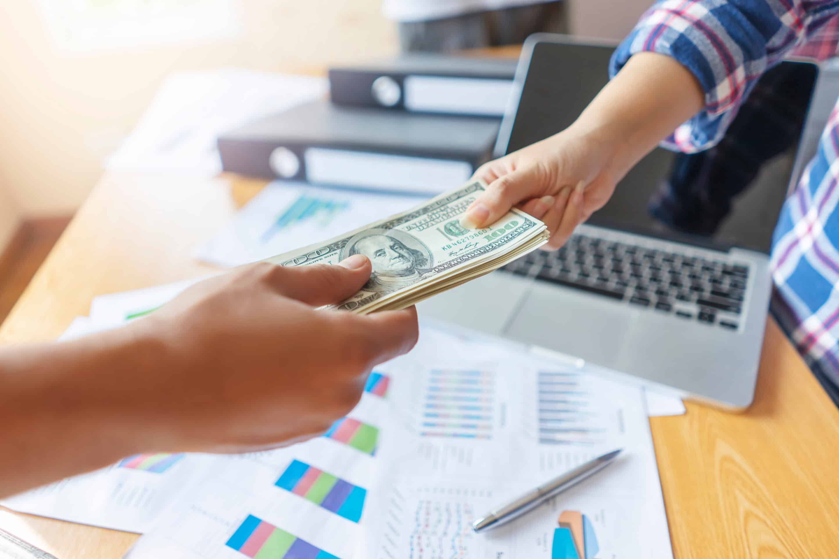 adobe stock - close up of businessman receiving money bills, representing getting paid monthly salary, across the desk from each other with wooden work desk with files, commuter laptop, pen and paper documentations close up of businessman receiving money bills, representing getting paid monthly salary, across the desk from each other with wooden work desk with files, commuter laptop, pen and paper documentations
