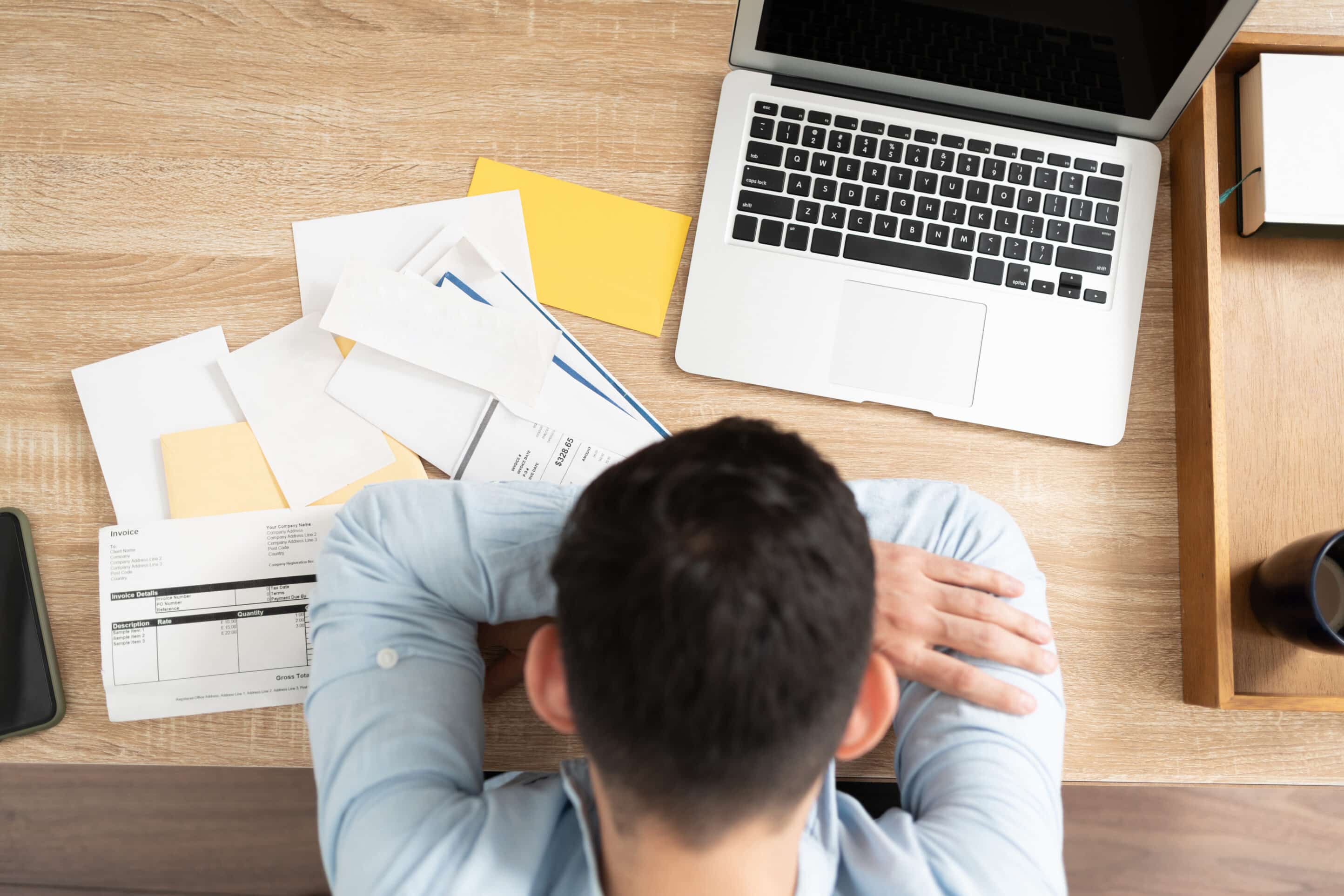 Man with a lot of debt feeling overwhelmed Top view of a broke man with a lot of debt giving up and feeling overwhelmed in front of too many bills
